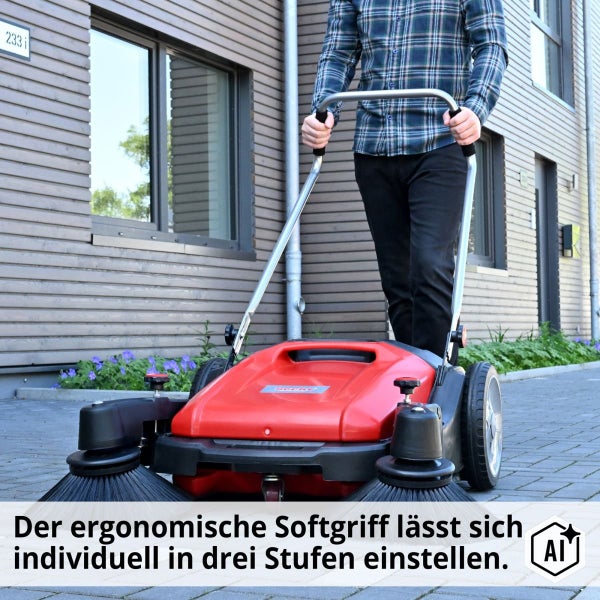 Person schiebt eine Kehrmaschine auf einem gepflasterten Weg vor einem Wohngebäude mit Hinweis auf den verstellbaren ergonomischen Softgriff.