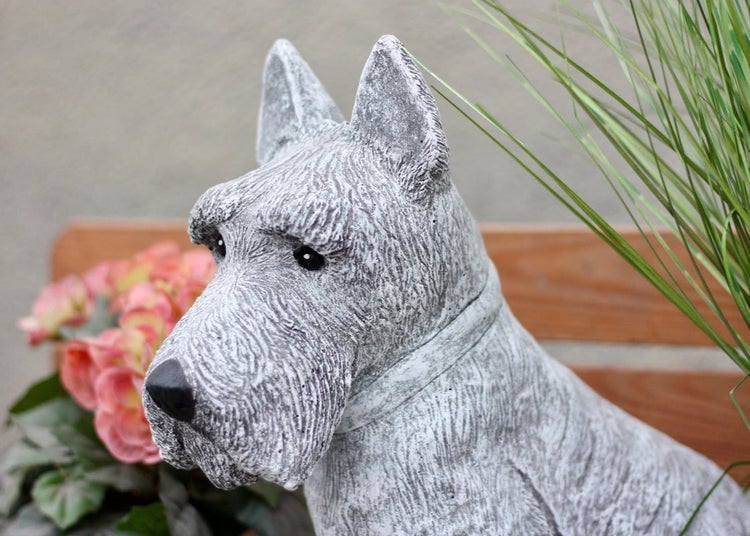 Gartenfigur Hund aus Steinguss, Motiv Schnauzer, dekorative Tierfigur für den Außenbereich neben einer Holzbank.