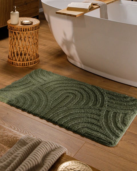 Grüner Badeteppich mit Wellenmuster auf Holzboden neben einer freistehenden Badewanne in einem hellen Badezimmer.