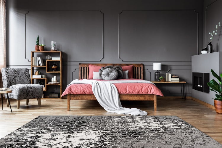 Modernes Schlafzimmer mit dunkelgrauer Wandvertäfelung, Holzbett mit rosa Bettwäsche, grauem Musterteppich und Holzregal auf hellem Holzboden.