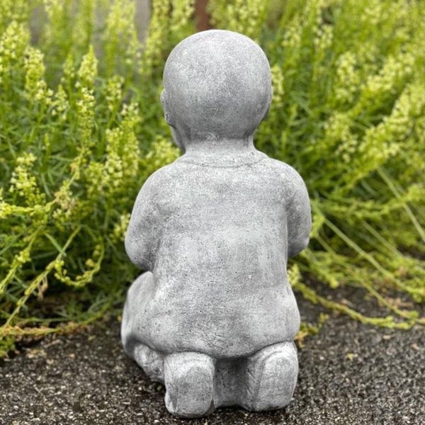 Gartenfigur Buddha aus Stein in sitzender Position vor einer Grünpflanze