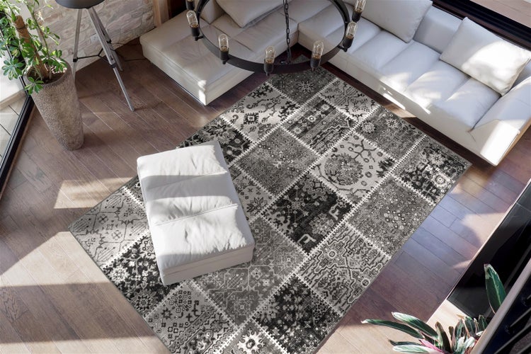 Patchwork-Teppich in Grau und Schwarz mit verschiedenen Mustern in einem hellen Wohnzimmer mit Sofa und Holzfußboden.