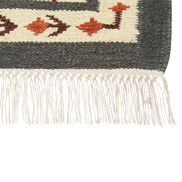 Detailansicht eines gewebten Teppichs mit geometrischem Muster in Grau, Creme, Orange und Braun mit Fransen.