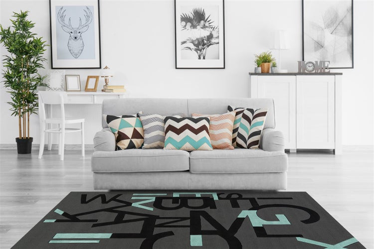 Modernes Wohnzimmer mit hellem Sofa, gemusterten Kissen und dunkelgrauem Teppich mit modernem Buchstabenmuster.