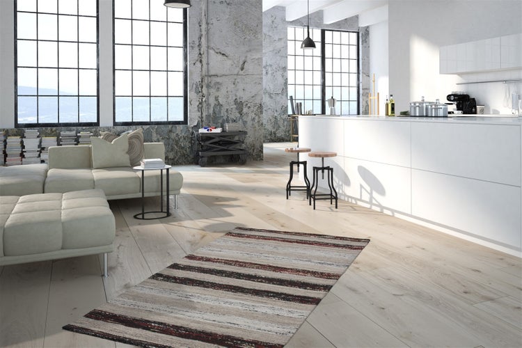 Heller Industrie-Loft mit offenem Küchen- und Wohnbereich, hellem Holzboden, weißer Kücheninsel und großen Industriefenstern.