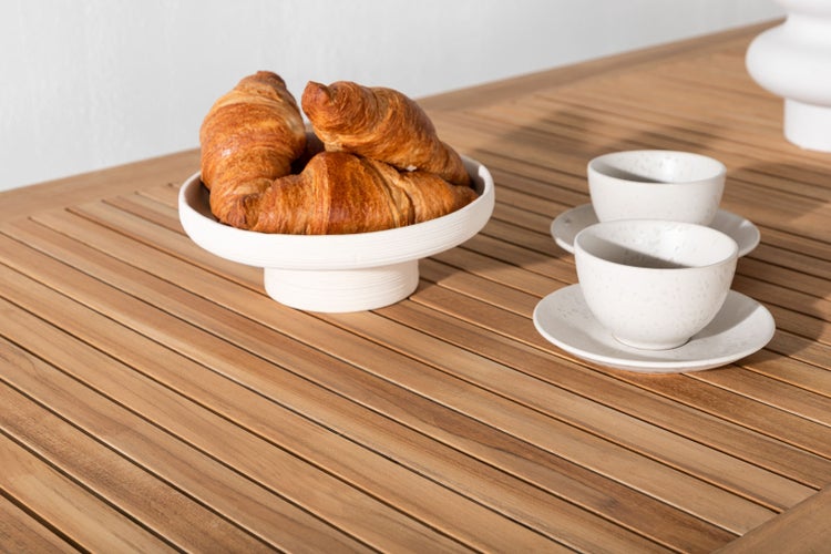 Gedeckter Holztisch mit Croissants in einer Schale und zwei Tassen mit Untertassen