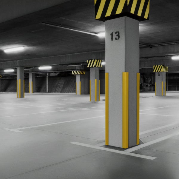 Eine Tiefgarage mit Betonpfeilern, gelben Schutzvorrichtungen und Parkplatzmarkierungen.