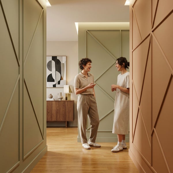 Zwei Frauen unterhalten sich in einem modernen Flur mit Wandpaneelen mit geometrischen Leisten, Parkettboden und einer Anrichte im Hintergrund.