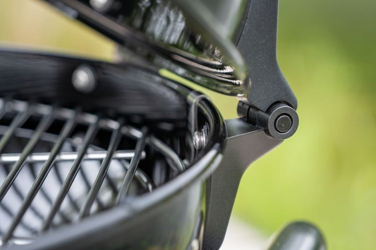 Detailansicht eines Grill-Deckelscharniers mit leicht geöffnetem Deckel und Grillrost.