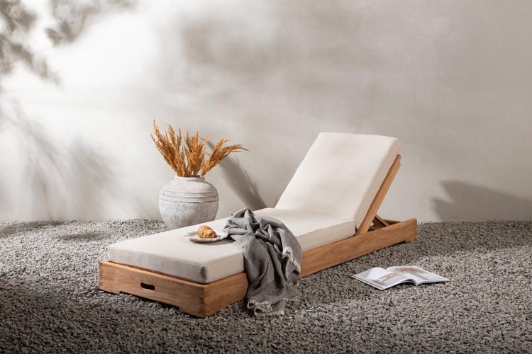 Szene mit einer Holzliege mit Polsterauflage, einem Überwurf, einem Croissant auf einem Teller, einer Vase mit Trockenblumen und einer Zeitschrift.