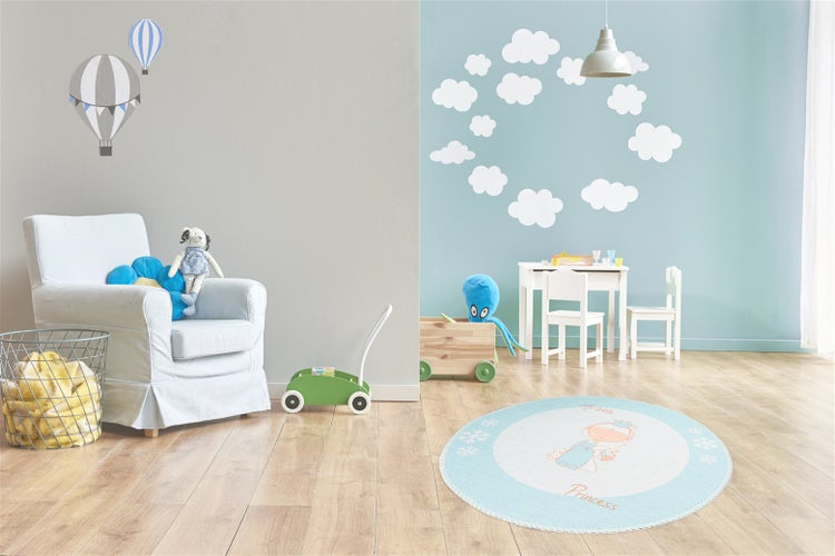 Helles Kinderzimmer mit Holzboden, weißem Sessel, Kindertisch mit Stühlen, rundem Teppich und Wandtattoos mit Wolken und Heißluftballons.