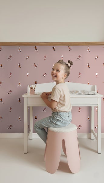 Mädchen sitzt an einem Schreibtisch vor einer Tapete mit Fußballmotiven