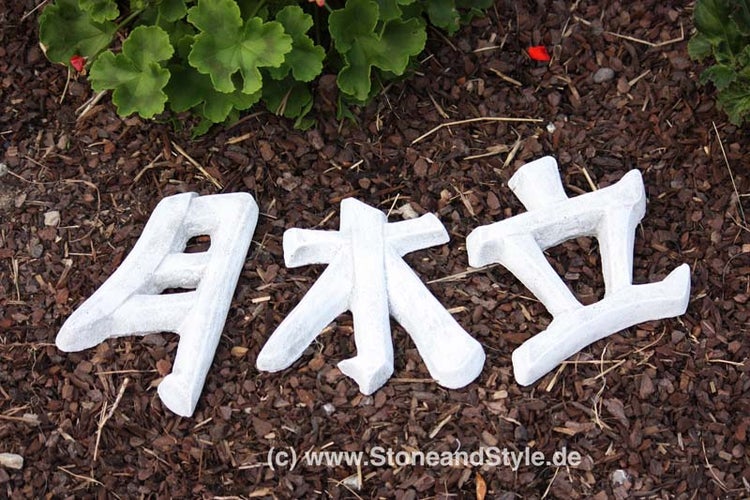 Drei asiatische Schriftzeichen als Dekoration aus Stein zur Gartengestaltung auf Rindenmulch.