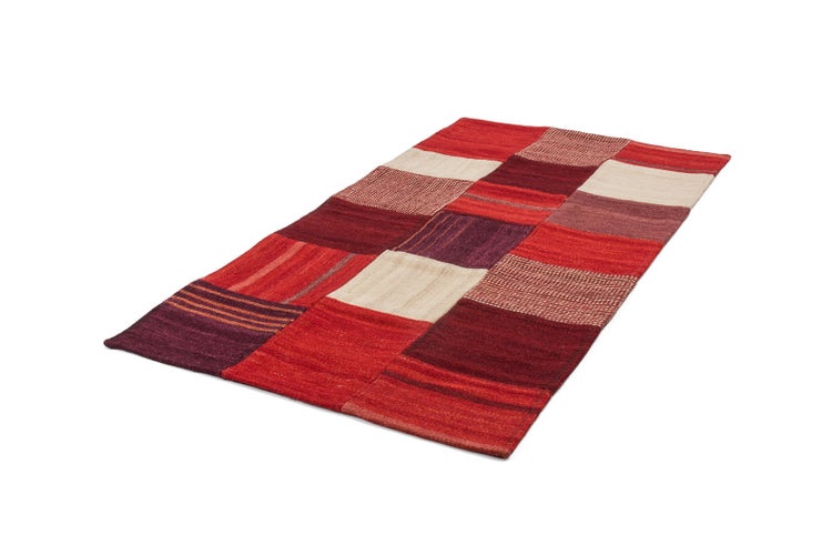 Patchwork-Teppich aus Stoffquadraten in verschiedenen Rot- und Beigetönen, rechteckig.