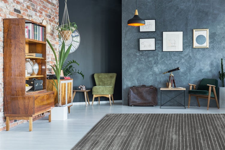 Moderner Wohnraum mit grau gestreiftem Teppich, Holzbücherregal vor Ziegelwand, grünen Sesseln und blau strukturierter Akzentwand.