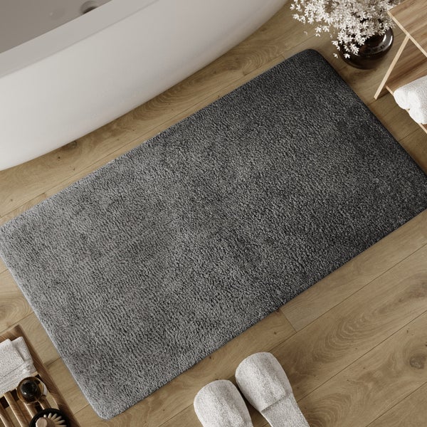 Flauschige Badematte in Anthrazit auf hellem Holzboden neben einer weißen Badewanne im modernen Badezimmer.