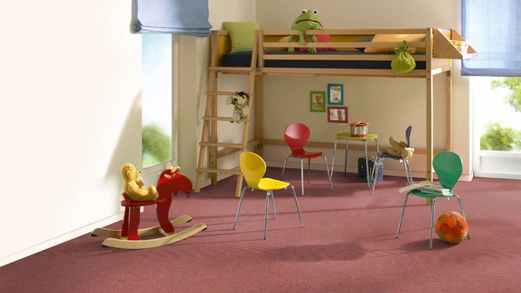 Helles, organisiertes Kinderzimmer mit Hochbett aus Holz, bunten Stühlen und verlegten Teppichfliesen auf dem Boden.