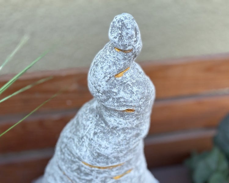 Nahaufnahme einer spiralförmigen Dekofigur in Steinoptik mit goldenen Akzenten für den Garten.