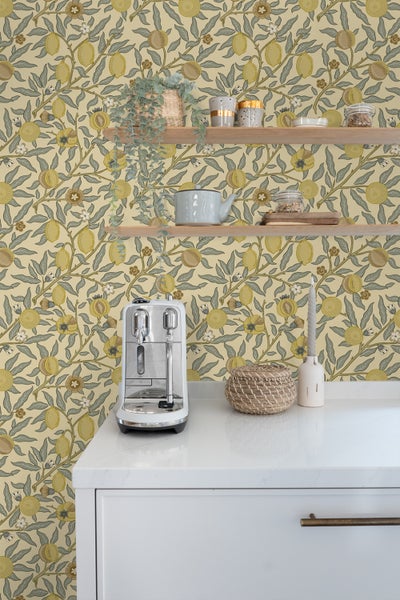 Küchenszene mit floraler Tapete, Regalen, Kaffeemaschine und dekorativen Elementen auf einer Arbeitsplatte.