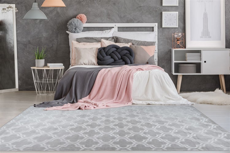 Modernes Schlafzimmer mit weißem Bett, strukturierter Wand und einem großen grauen Teppich mit weißem Muster im Vordergrund.
