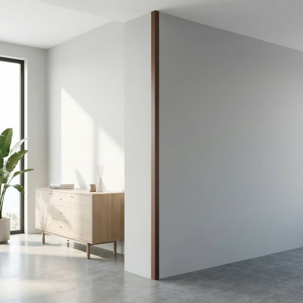 Heller Wohnraum mit einer Eckleiste an der Wand, einem Sideboard aus Holz und einer Pflanze vor einem bodentiefen Fenster.