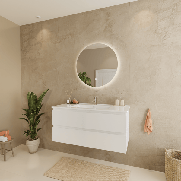 Modernes Badezimmer mit hängendem weißem Waschtischunterschrank, integriertem Waschbecken und rundem beleuchtetem Spiegel an strukturierter Wand.