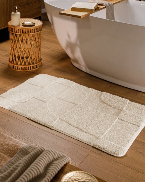 Rechteckige Badematte mit geometrischem Reliefmuster in einem hellen Badezimmer vor einer freistehenden Badewanne auf Holzfußboden.