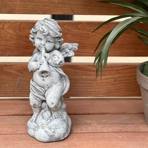 Steinfigur Engel mit Trompete als Gartendekoration aus Kunststein auf einem Holzuntergrund.