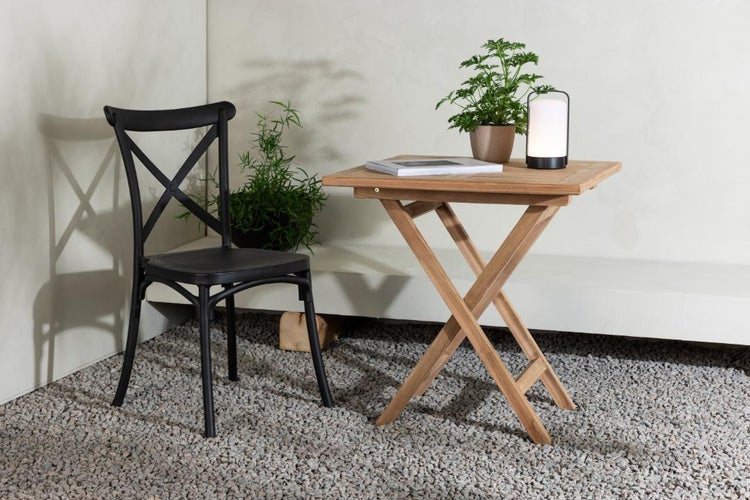 Szene mit einem schwarzen Stuhl mit Kreuzstreben, einem klappbaren Holztisch, einer Lampe und Pflanzen im Topf.