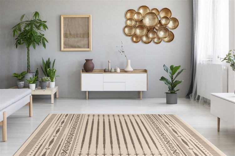 Ein helles, aufgeräumtes Wohnzimmer mit einem gewebten Teppich mit geometrischem Muster, einem Sideboard, Wanddeko und Zimmerpflanzen.