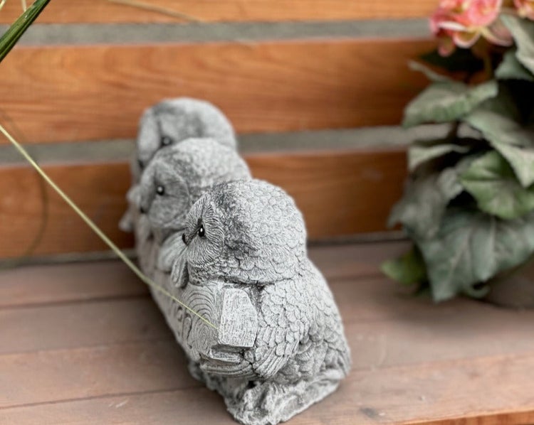 Dekorative Gartenfigur aus Stein mit drei nebeneinander auf einem Ast sitzenden Eulen.