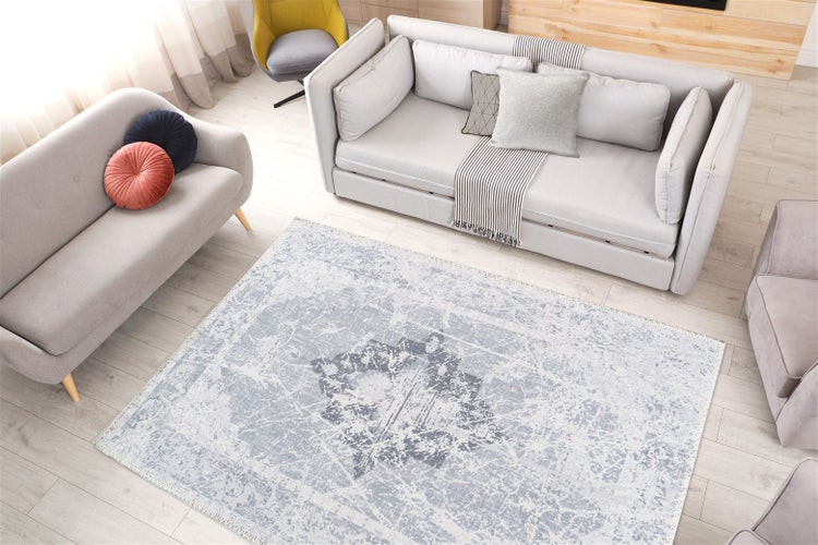 Rechteckiger Teppich mit hellblauem Vintage-Muster auf hellem Holzboden in einem hellen Wohnzimmer mit grauen Sofas.