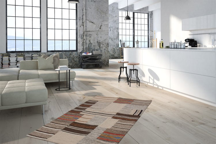 Moderner Wohnbereich im Industriedesign mit hellem Holzfußboden, Sofa und gemustertem Teppich vor einer weißen Kücheninsel.