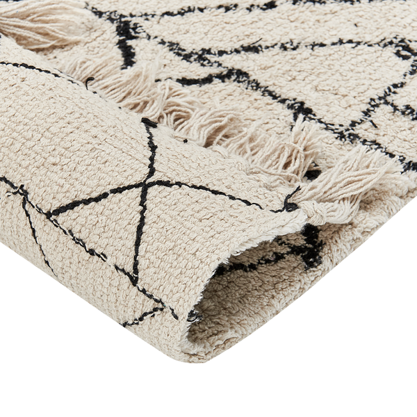 Nahaufnahme eines Hochflor-Teppichs mit schwarzem geometrischem Linienmuster, Fransen und einer umgeschlagenen Ecke.