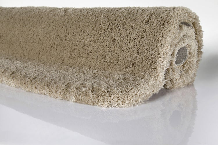 Teilweise aufgerollter Hochflor Teppich mit weicher Struktur in Beige.