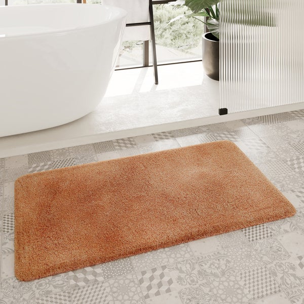 Rechteckige orangefarbene Badematte mit weicher Textur auf gemusterten Fliesen in einem hellen Badezimmer neben einer Badewanne.