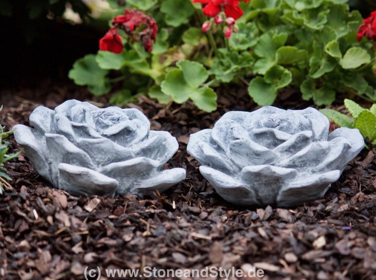 Zwei dekorative Rosenfiguren aus Stein zur Gartendekoration in einem Beet.