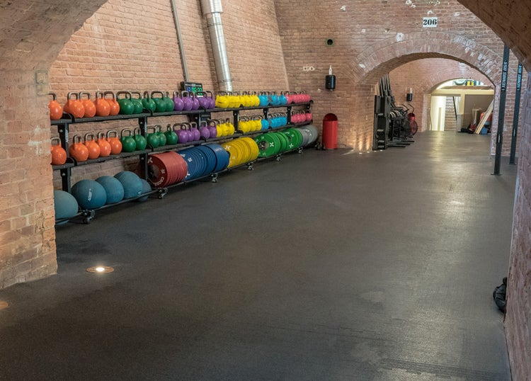 Innenaufnahme eines Fitnessstudios mit Hanteln, Kugelhanteln und Medizinbällen auf Regalen unter einem Ziegelsteingewölbe