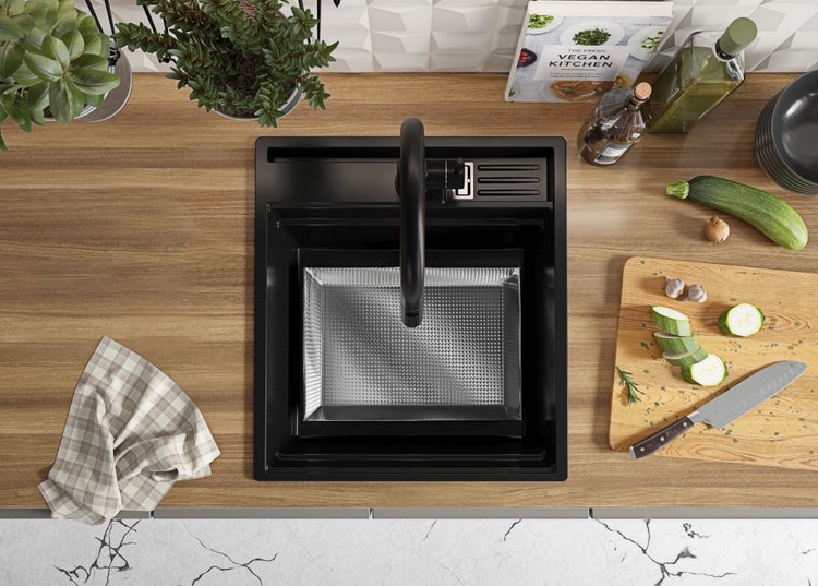 Küchenszene mit Spüle, Armatur, Schneidebrett, Messer, Gemüse, Kräutern und Kochbuch