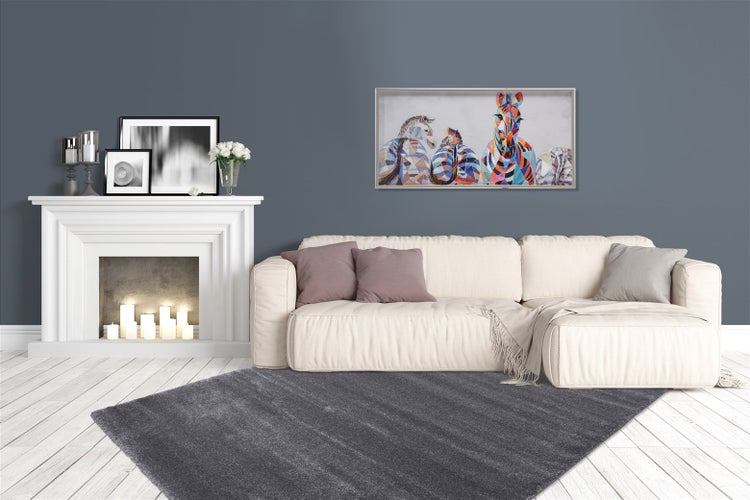 Modernes Wohnzimmer mit hellem Sofa, dunkelgrauem Teppich, weißem Dekokamin mit Kerzen und farbenfrohem Wandbild.