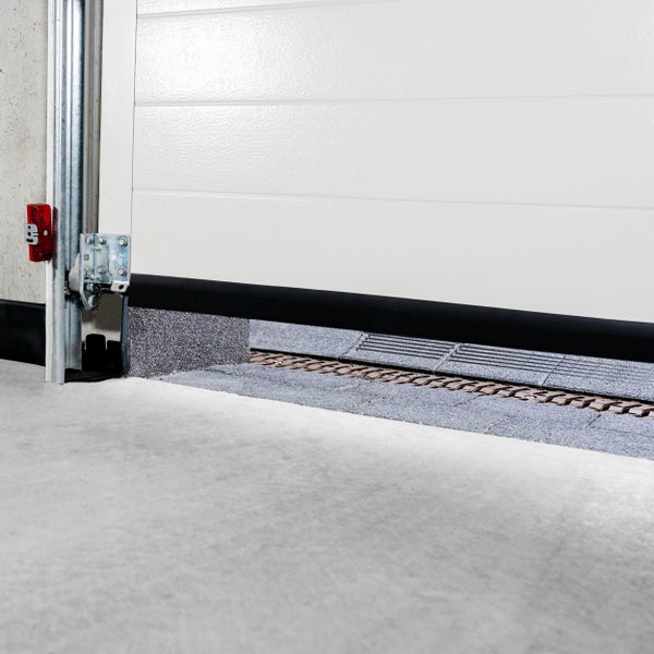 Detailansicht eines leicht geöffneten, weißen Garagentors mit Führungsschiene und Bodenablauf