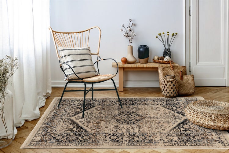 Vintage-Orientteppich mit beige-blauem Muster in einem hellen Wohnzimmer mit Rattan-Sessel, Holzbank und geflochtenem Sitzkissen.