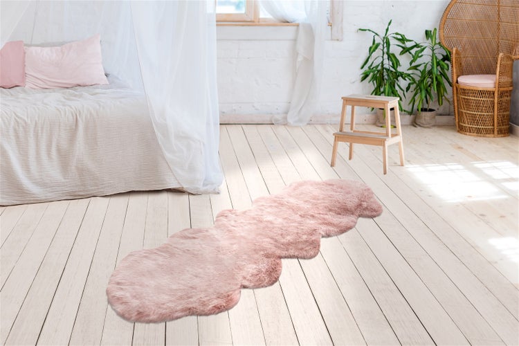 Rosafarbener Kunstfell-Läufer in hellem Schlafzimmer auf Holzdielen mit Bett, Zimmerpflanzen und Trittleiter aus Holz.