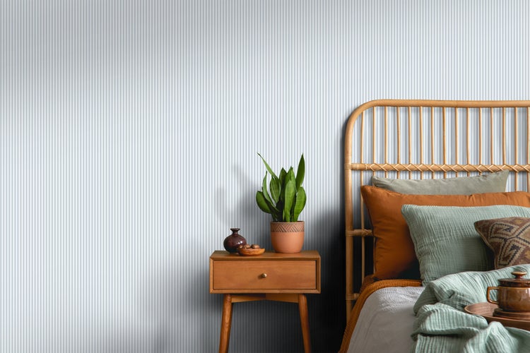 Schlafzimmer mit Rattanbett, Nachttisch und gestreifter Tapete für eine helle und organisierte Atmosphäre.