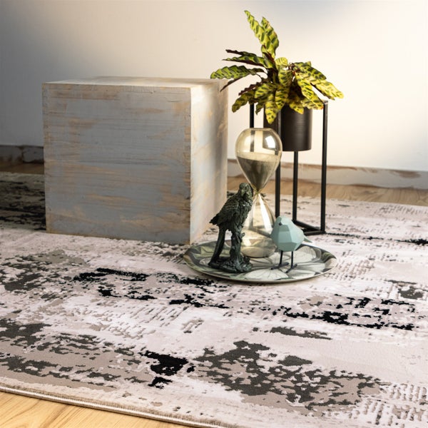 Moderner Teppich mit abstraktem Muster in Grau und Beige. Im Raum stehen ein Holzwürfel, Pflanzenständer und Dekorationsfiguren auf einem Teller.