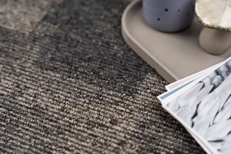 Nahaufnahme eines strukturierten Schlingenteppichs in Grau und Beige mit dekorativen Wohnaccessoires.