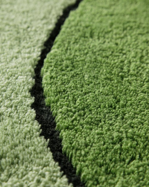 Nahaufnahme eines weichen grünen Hochflor-Teppichs mit geschwungenem Muster.