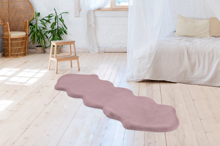 Länglicher, gewellter Kunstfellteppich in einem hellen Schlafzimmer mit Holzdielenboden, Bett und Zimmerpflanzen.