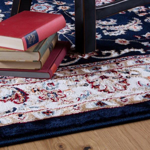 Blauer orientalischer Teppich mit floralem Muster und dichtem Flor auf einem Holzboden mit Büchern und einem Möbelfuß.