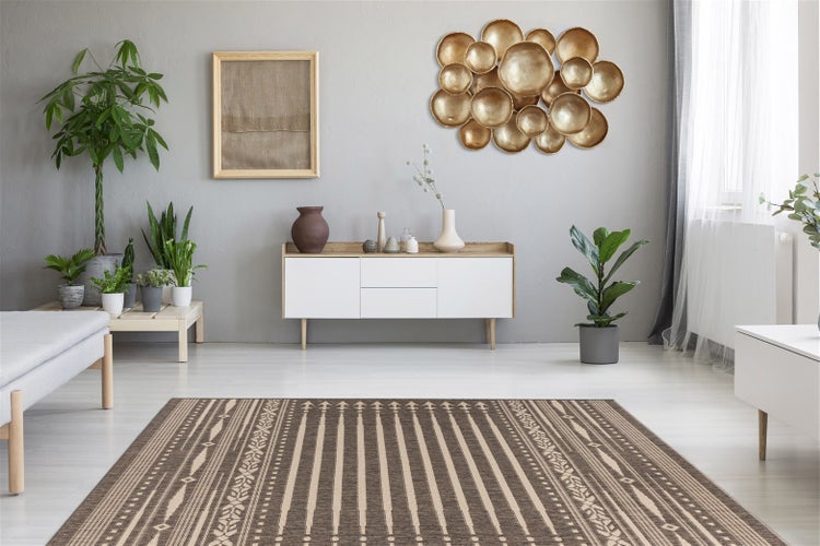 Modernes Wohnzimmer mit gemustertem Teppich in Braun und Beige, weißem Sideboard, Zimmerpflanzen und goldener Wanddekoration vor grauer Wand.